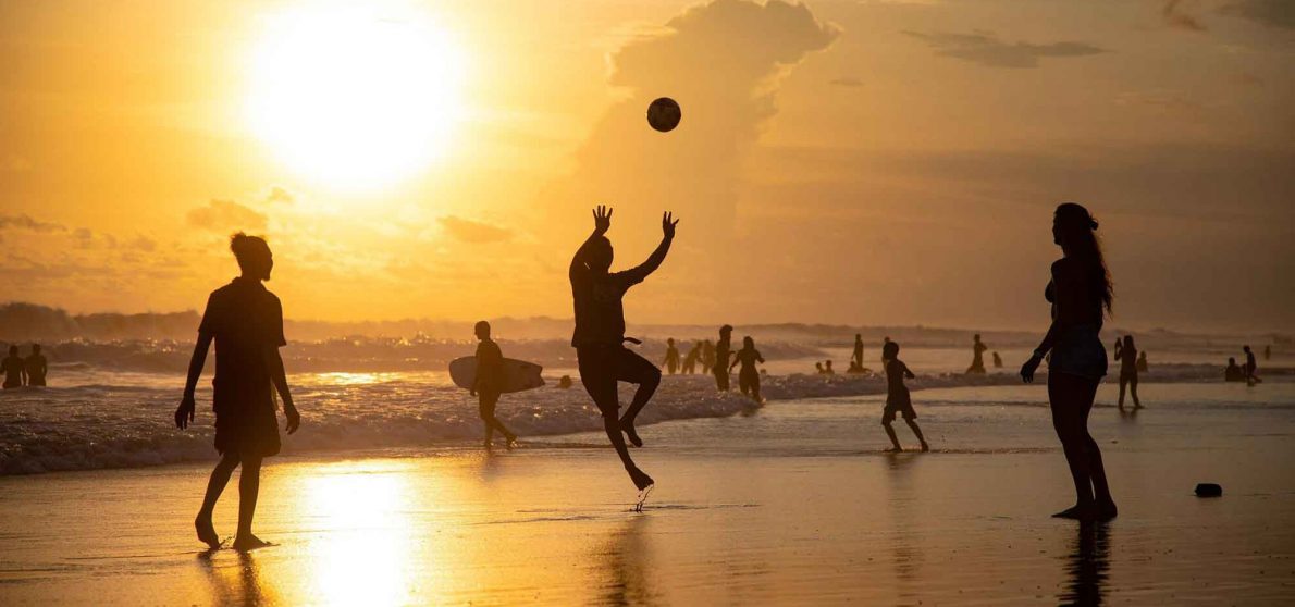 des gens jouent au volley sur la plage alors que le soleil se couche