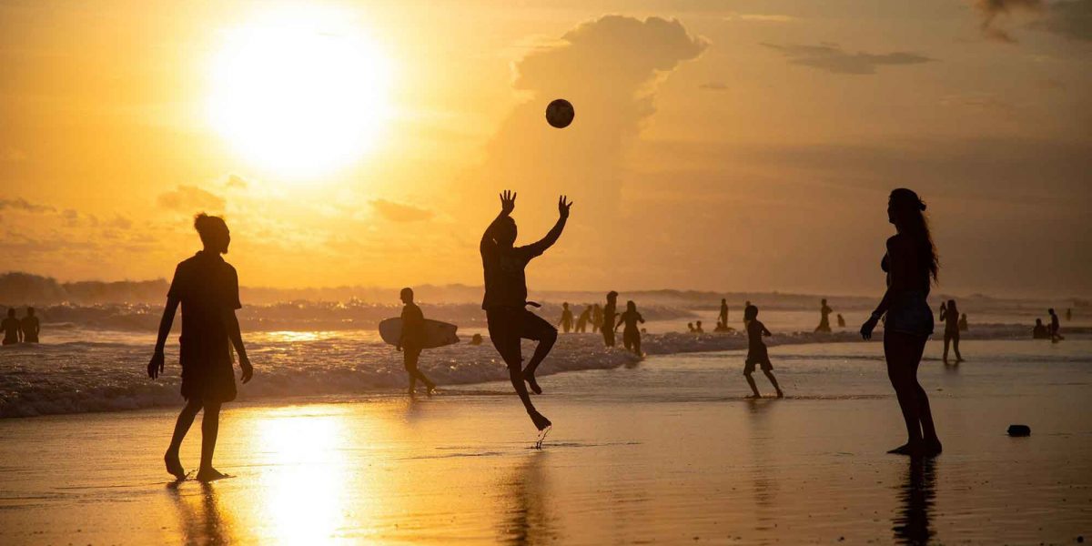 des gens jouent au volley sur la plage alors que le soleil se couche