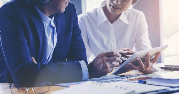 Young attractive businesswoman working with touchpad has been guided and consulting by senior colleague