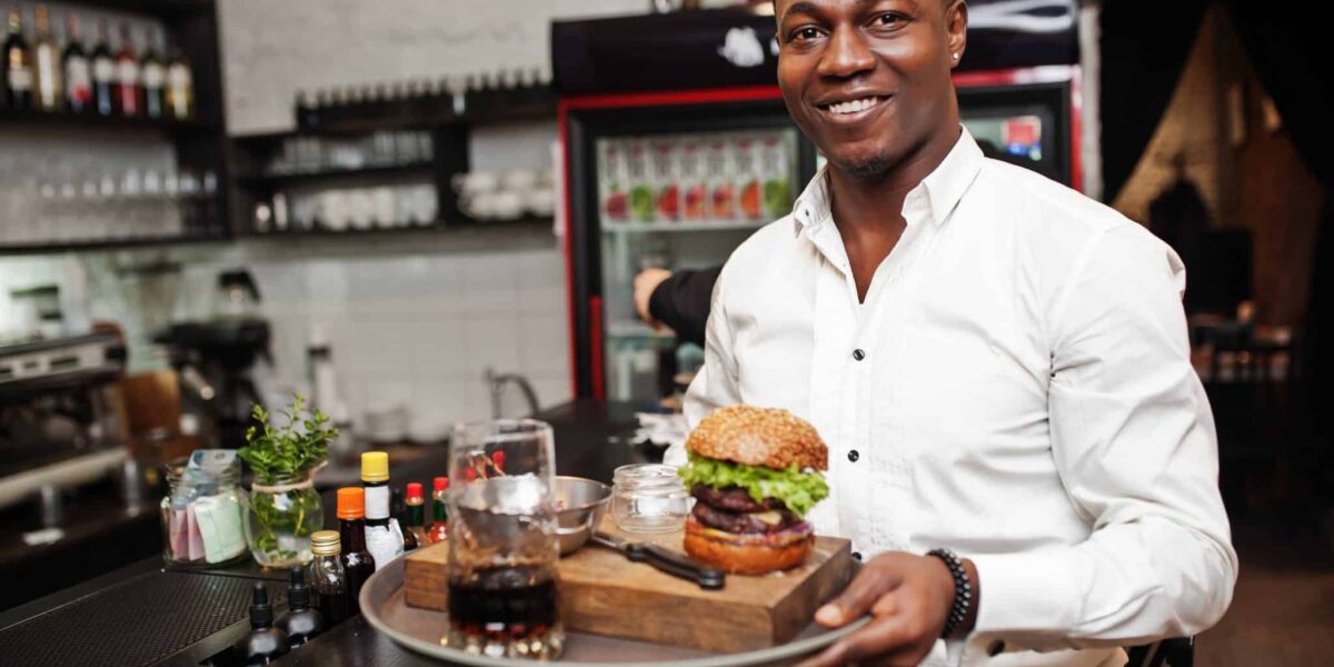 Young african american waiter man hold tray with burger at bar of restaurant.